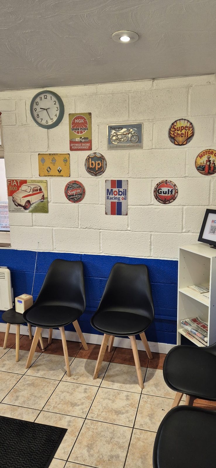 Our customer waiting area, with black chairs, a clock and vintage oil and fuel signs on the wall
