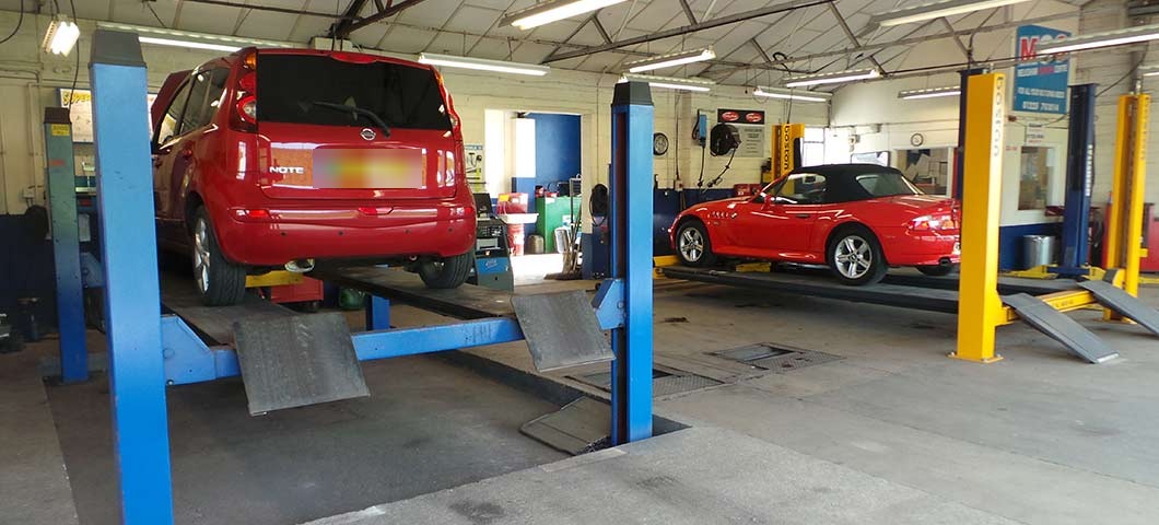 Inside the workshop: a car raised on a blue two-post lift and a red roadster on a four-post lift