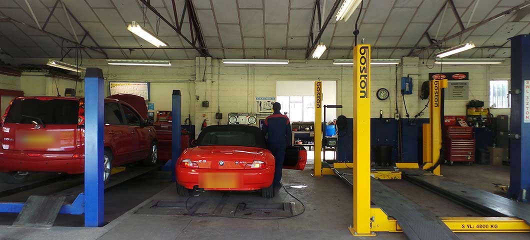 Technician at work beside the yellow lifts, with a red roadster and a hatchback raised in the bays
